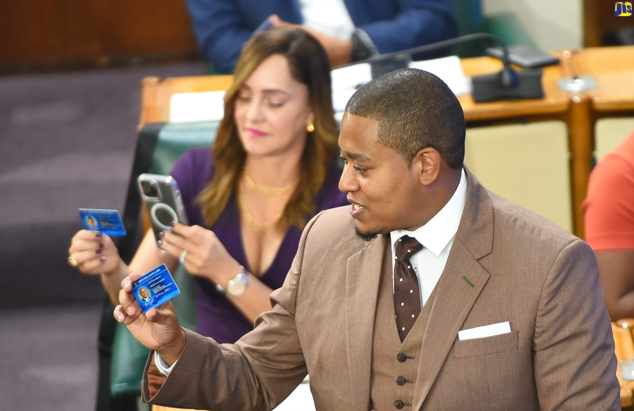 Minister without Portfolio in the Office of the Prime Minister, Hon. Floyd Green (foreground), displays one of the digital cards he issued during his contribution to the 2022/23 Sectoral Debate in the House of Representatives on Tuesday (May 24). The ‘Sectoral’ cards feature a QR Code that can be scanned to access his full presentation.  Member of Parliament for Portland Eastern, Ann-Marie Vaz (background), scans the code with her smart phone.