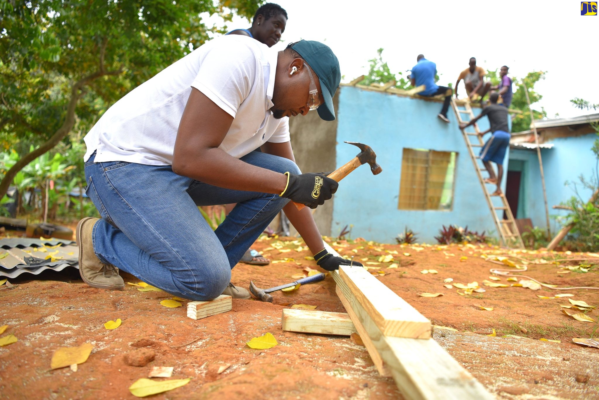 Member of Parliament (MP) for Clarendon North Central and Minister without Portfolio in the Office of the Prime Minister (OPM), with responsibility for Information, Hon. Robert Morgan, drives a nail into support boards to be placed on the roof of a family’s house (pictured in the background) in Mocho Clarendon. The Minister was participating in the main Labour Day project in the constituency on Monday (May 23). The project entailed replacing the entire roof of the dwelling, which had previously leaked.  