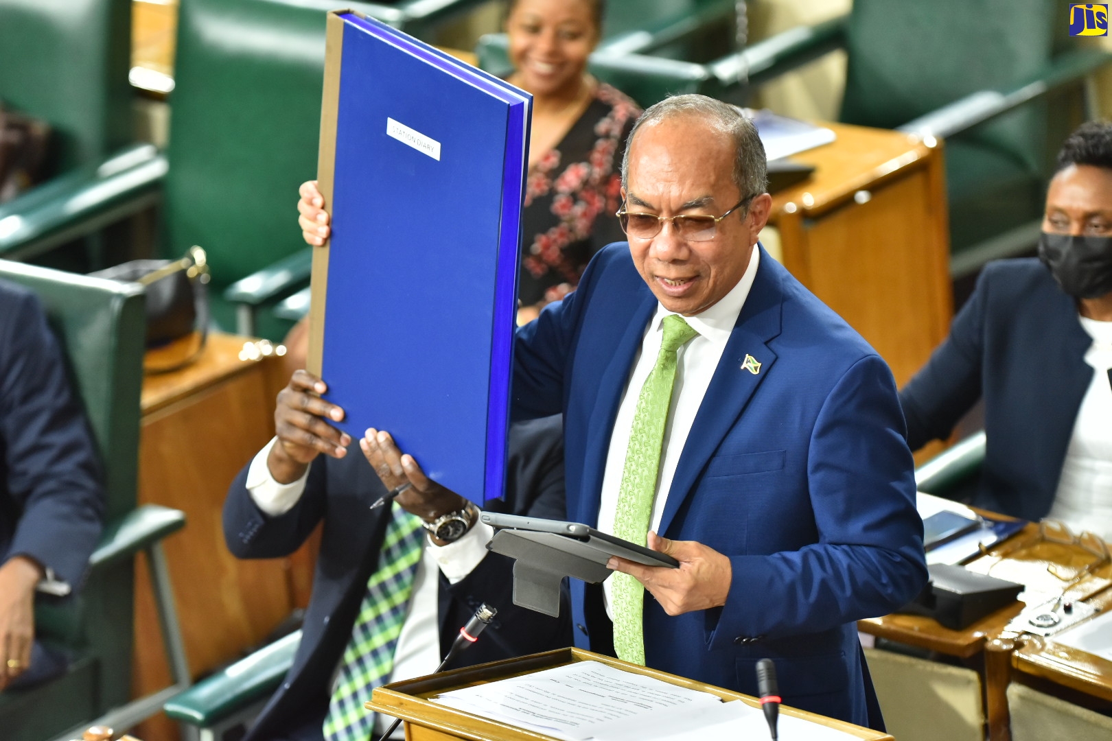 Minister of National Security and Deputy Prime Minister, Hon. Dr. Horace Chang, is assisted by State Minister in the Ministry, Hon. Zavia Mayne (seated left), in displaying a manual station diary during his contribution to the 2022/23 Sectoral Debate in the House of Representatives on June 1. The Government is replacing these big books with an electronic records system.