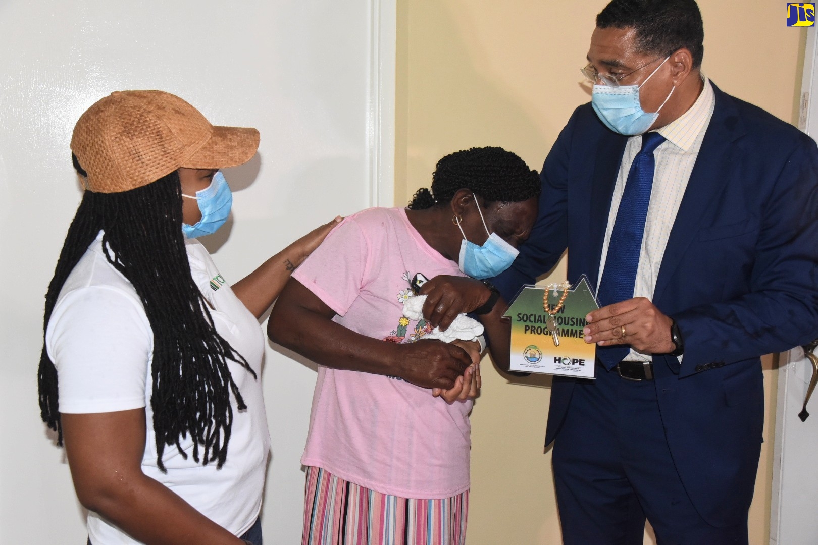 Prime Minister, the Most Hon. Andrew Holness, consoles Brenda Grant who was overcome with emotions after receiving the keys to her new three-bedroom house, constructed under the New Social Housing Programme (NSHP) in Wakefield Trelawny. Sharing in the moment is Member of Parliament for Trelawny Northern, Tova Hamilton. The unit, constructed at a cost of $6.5 million, was handed over to Ms. Grant during a ceremony held on Friday (June 18)