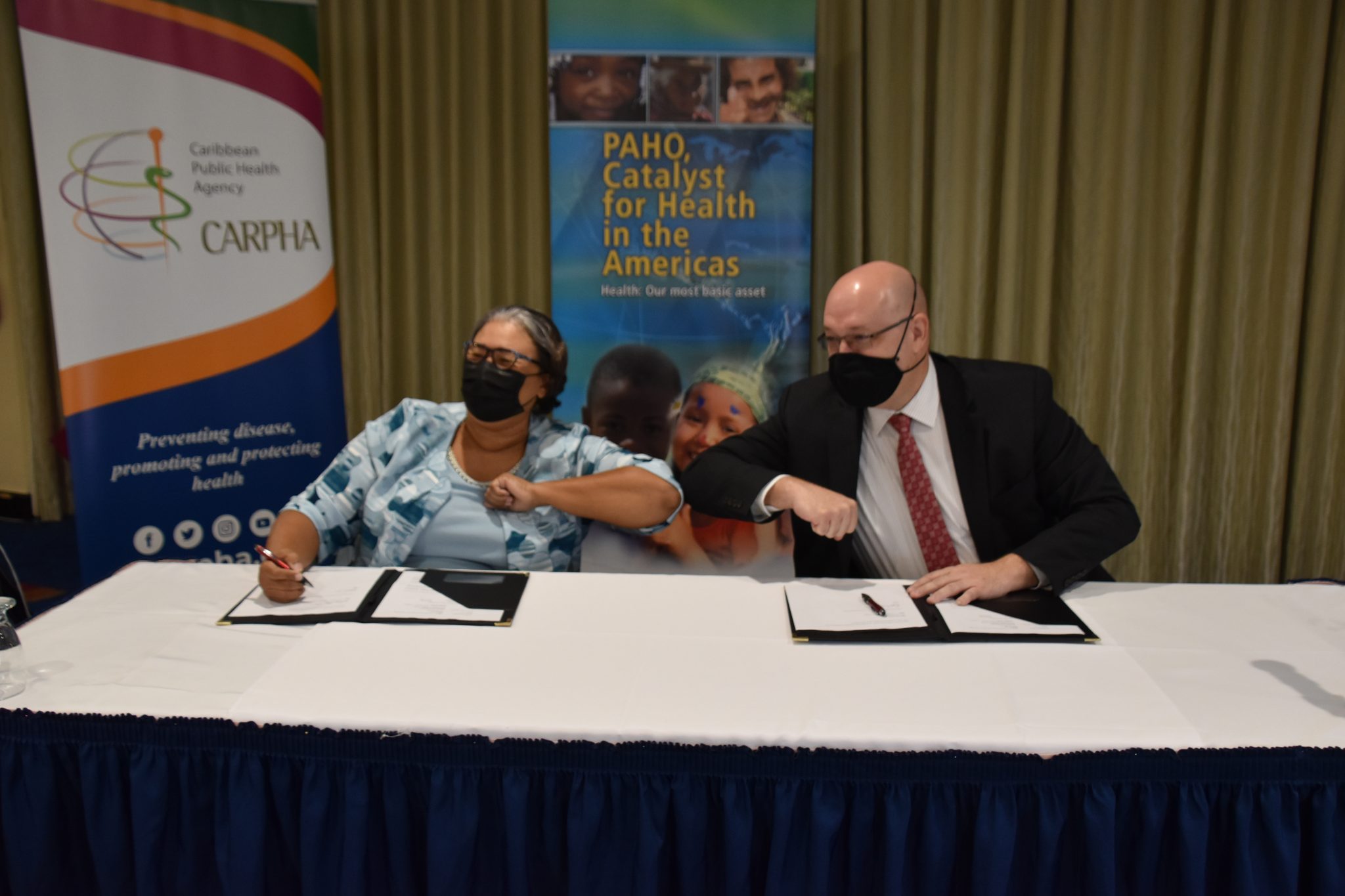 Executive Director, Caribbean Public Health Agency (CARPHA), Dr. Joy St. John (left), and Pan American Health Organization (PAHO) Sub-Regional Programme Director, Dean Chambliss, bump elbows after signing a US$750,000 subsidiary agreement at CARPHA’s headquarters in Trinidad and Tobago.