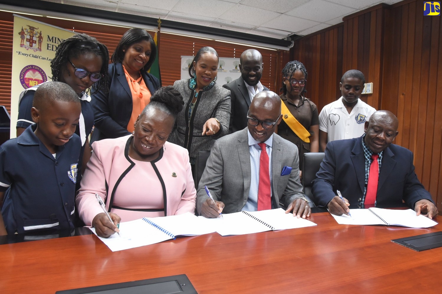 A Memorandum of Understanding (MOU) for the adoption of the Savanna la-Mar Primary School in Westmoreland was signed by representatives of Dreams To Reality (DTR) Foundation,  Dequity Capital Management and the school, at the Ministry of Education and Youth in Kingston on Thursday (July 28). Acting Chief Education Officer in the Ministry, Dr. Kasan Troupe (standing fourth left), points out something of interest, while (seated from left) Principal of Savanna-la-Mar Primary, Megan Berry; Chairman, DTR Foundation, Garold Hamilton; and school board Chairman, Laumond Senior, affix their signatures to the agreement. Also looking on (standing from left) are students Andrew Romans and Emily Palmer; Executive Director of the National Education Trust (NET), Latoya Harris; Chief Executive Officer, Dequity Capital Adrian Smith; and students De’Asia Thomas and Shevoy Reynolds. 