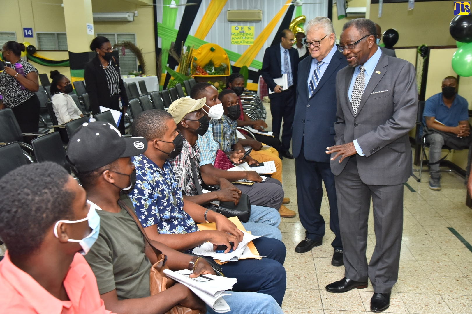 Minister of Labour and Social Security, Hon. Karl Samuda (second left), listens as United States (US) Ambassador to Jamaica, His Excellency Nick Perry (right), extends well wishes to workers prior to their departure from the Ministry’s Overseas Employment Centre on East Street in downtown Kingston, on Thursday (July 28), for the Norman Manley International Airport in Kingston, en route to the US, to participate in the seasonal farm-work programme.