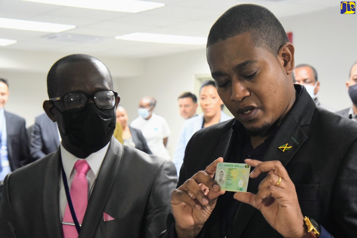 Minister without Portfolio in the Office of the Prime Minister, Hon. Floyd Green (right), displays a specimen of the National Identification Card during a tour of the enrolment centre at the Central Sorting Office on South Camp Road in Kingston on Thursday (August 11). Looking on is Programme Director of the National Identification System (NIDS), Dr. Warren Vernon.