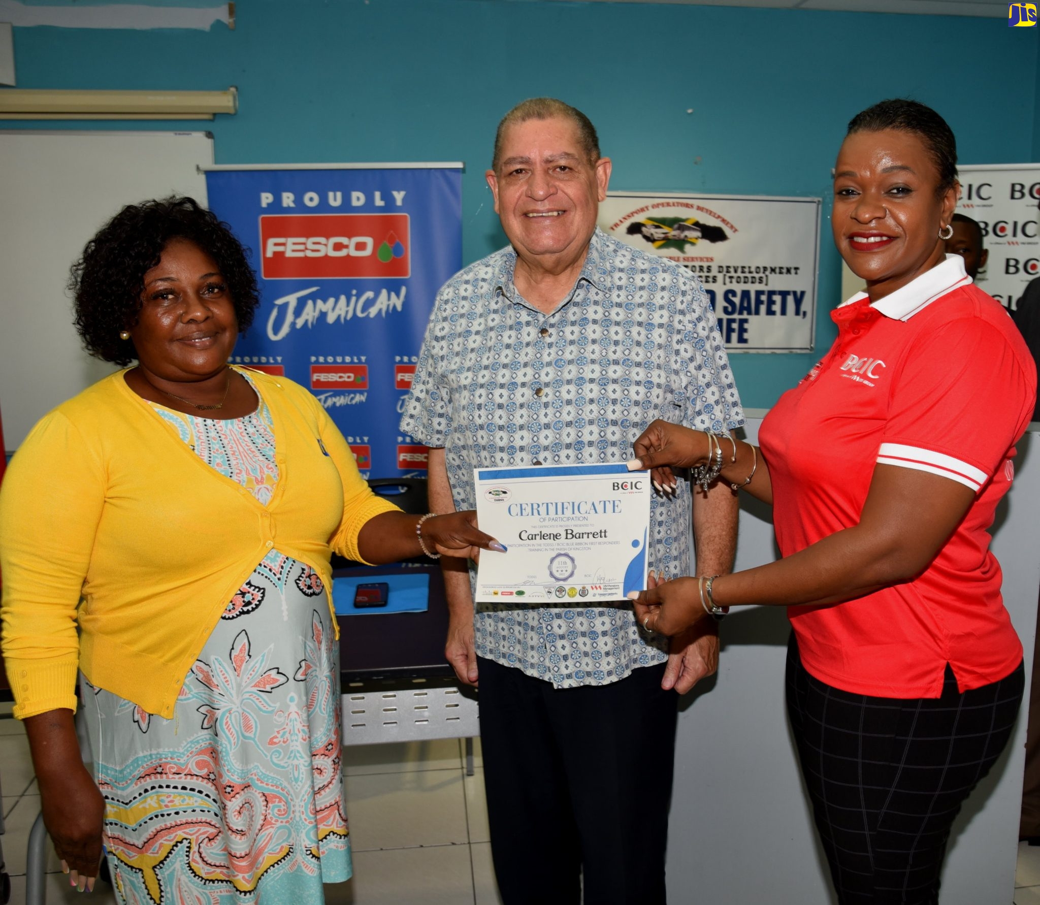 Minister of Transport and Mining, Hon. Audley Shaw, observes as participant in the Blue Ribbon First Responders Training, Carlene Barrett (left), receives her certificate from Chief Operating Officer at British Caribbean Insurance Company, Michelle Anderson. The presentation ceremony was held at the University of Technology, Jamaica, on Thursday, August 11