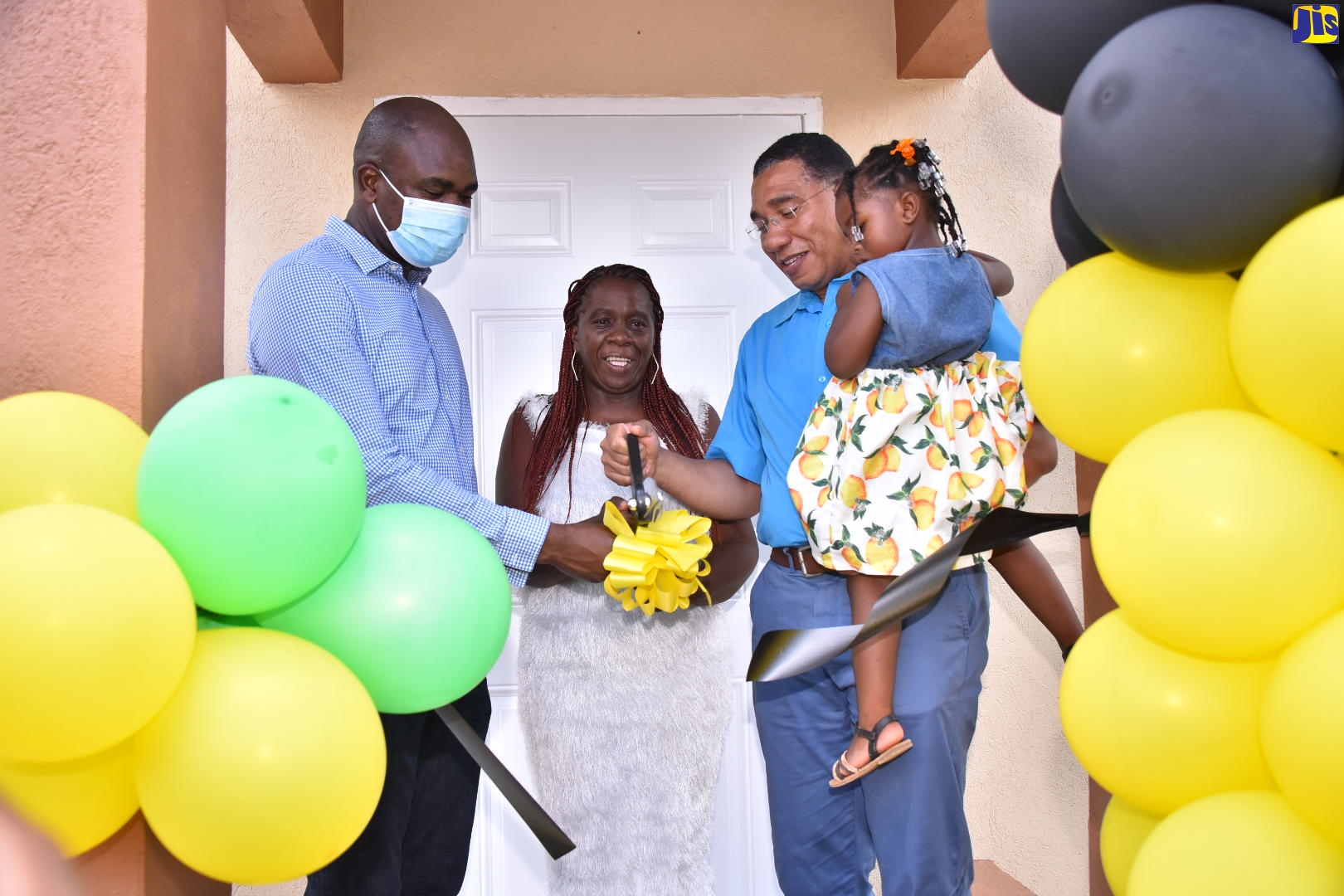 Prime Minister, the Most Hon. Andrew Holness (right), cuts the ribbon to officially hand over a new two-bedroom unit to New Social Housing Programme (NSHP) beneficiary, Sophia Campbell (centre), in Cave Valley, St. Ann, on August 19. Assisting the Prime Minister is Minister of State in the Ministry of National Security, Hon. Zavia Mayne, who is also Member of Parliament for St. Ann South West. Ms.  Campbell’s granddaughter, Zahara Walker, is being held by Mr. Holness. 