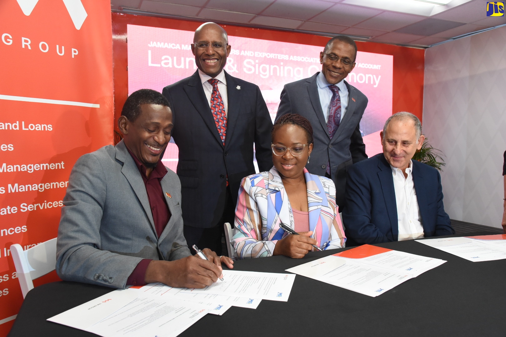 Minister of Industry, Investment and Commerce, Senator the Hon. Aubyn Hill (left, standing), looks on as Chief Executive Officer, Victoria Mutual (VM) Pensions Management Limited, Conroy Rose (left, seated), signs a partnership agreement between the entity and the Jamaica Manufacturers and Exporters Association (JMEA) to provide special pension solutions to the JMEA member companies and their employees. The signing took place during the initiative’s launch at the Victoria Mutual Building Society (VMBS) on Half-Way Tree Road in Kingston, on Tuesday (September 6). Looking on are JMEA Executive Director, Kamesha Blake (centre, seated), and President, JMEA, John Mahfood (right, seated), and VMBS Group President and Chief Executive Officer, Courtney Campbell.