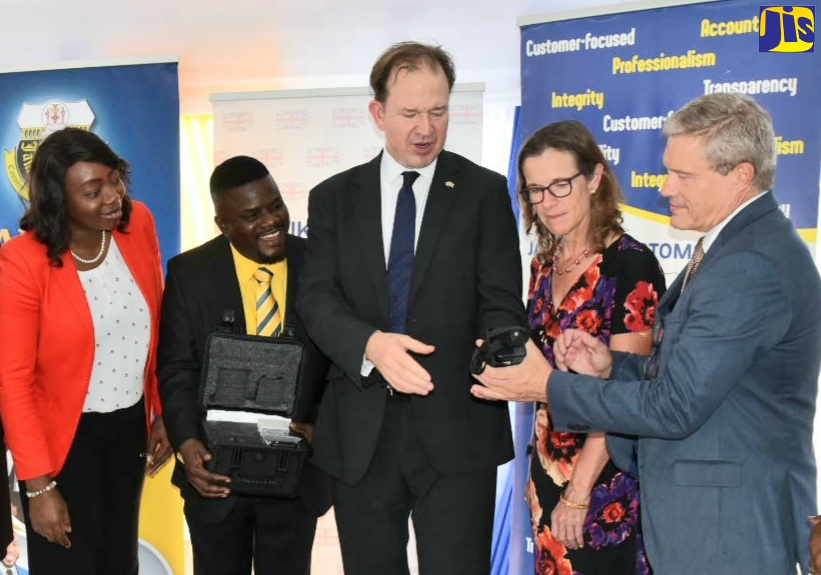 United Kingdom (UK) Minister for the Americas and Overseas Territories, Hon. Jesse Norman (centre) is handed a Buster Density Meter by First Secretary of Border Force International-Jamaica with the British High Commission, Michael Gorrie (right). Several of the devices, donated by the UK Government, were handed over during a ceremony on Tuesday (October 25) at the Jamaica Customs Agency (JCA) head office, Newport East, Kingston. Looking on (from left) are Acting Deputy Commissioner of Operations, JCA, Selina Clarke-Graham; Deputy Chief Executive Officer of Border Protection, JCA, Marlon Lowe; and British High Commissioner to Jamaica, Her Excellency Judith Slater. The donation is part of the ongoing UK-Jamaica collaboration to tackle the issue of arms smuggling. 