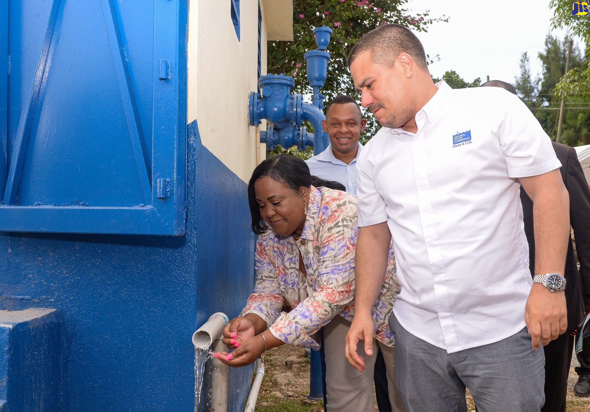 Minister Without Portfolio in the Ministry of Economic Growth and Job Creation, Senator the Hon. Matthew Samuda (right), looks on as Member of Parliament, St. Catherine North Central, Natalie Neita-Garvey (left), uses water supplied by the National Water Commission’s (NWC’s) upgraded Sligoville water system, during the facility’s recent commissioning. With them is NWC Vice President for Operations, Kevin Kerr.