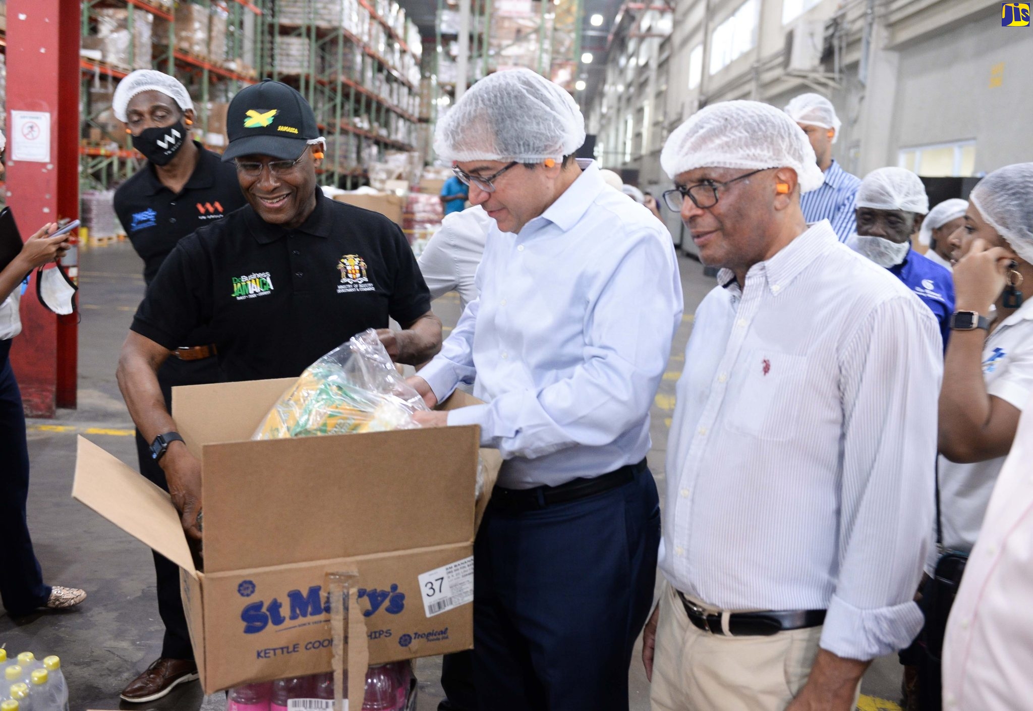 Minister of Industry, Investment and Commerce, Senator the Hon. Aubyn Hill (second left), assists Wisynco Group Chief Executive Officer, Andrew Mahfood (second right), with a package of St. Mary Banana Chips, which is distributed by the entity’s Lakes Pen facility in St. Catherine, during a tour of the plant, on Wednesday (November 9). At right is Wisynco’s Director of Manufacturing, Devon Reynolds.  