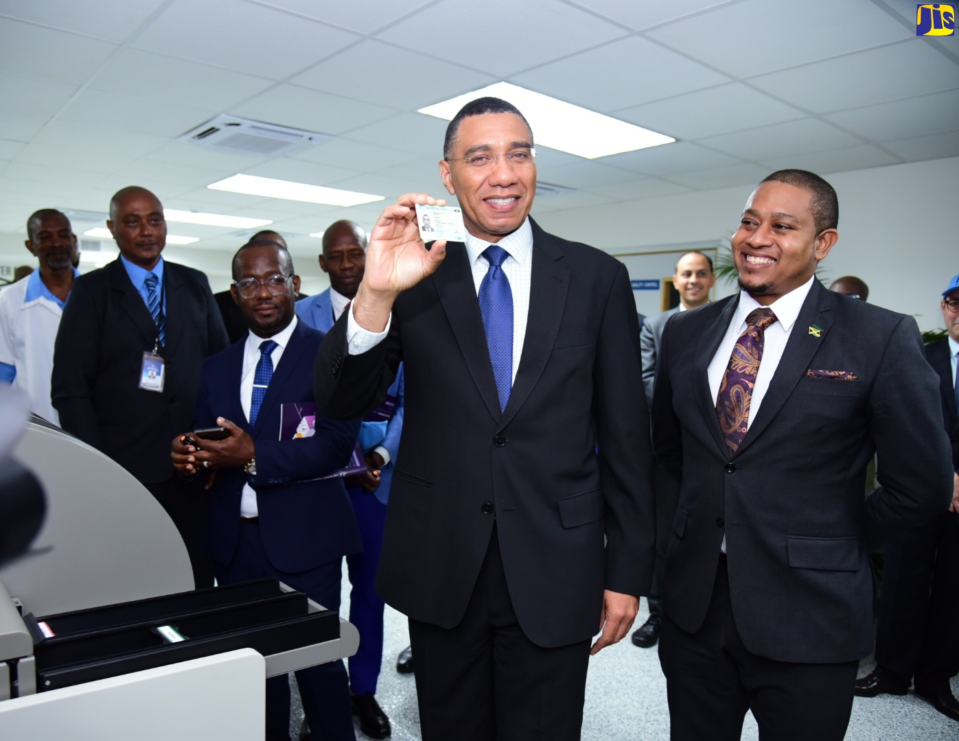 (FILE) Prime Minister, the Most Hon. Andrew Holness (second right), displays a copy of his newly printed national identification card, as he toured the Enrolment and Card Personalisation Centre located at the Jamaica Post Central Sorting Office in Kingston on Tuesday (December 13). Looking on (from left) are Programme Director of the National Identification System (NIDS), Dr. Warren Vernon, and Minister without Portfolio in the Office of the Prime Minister, Hon. Floyd Green.