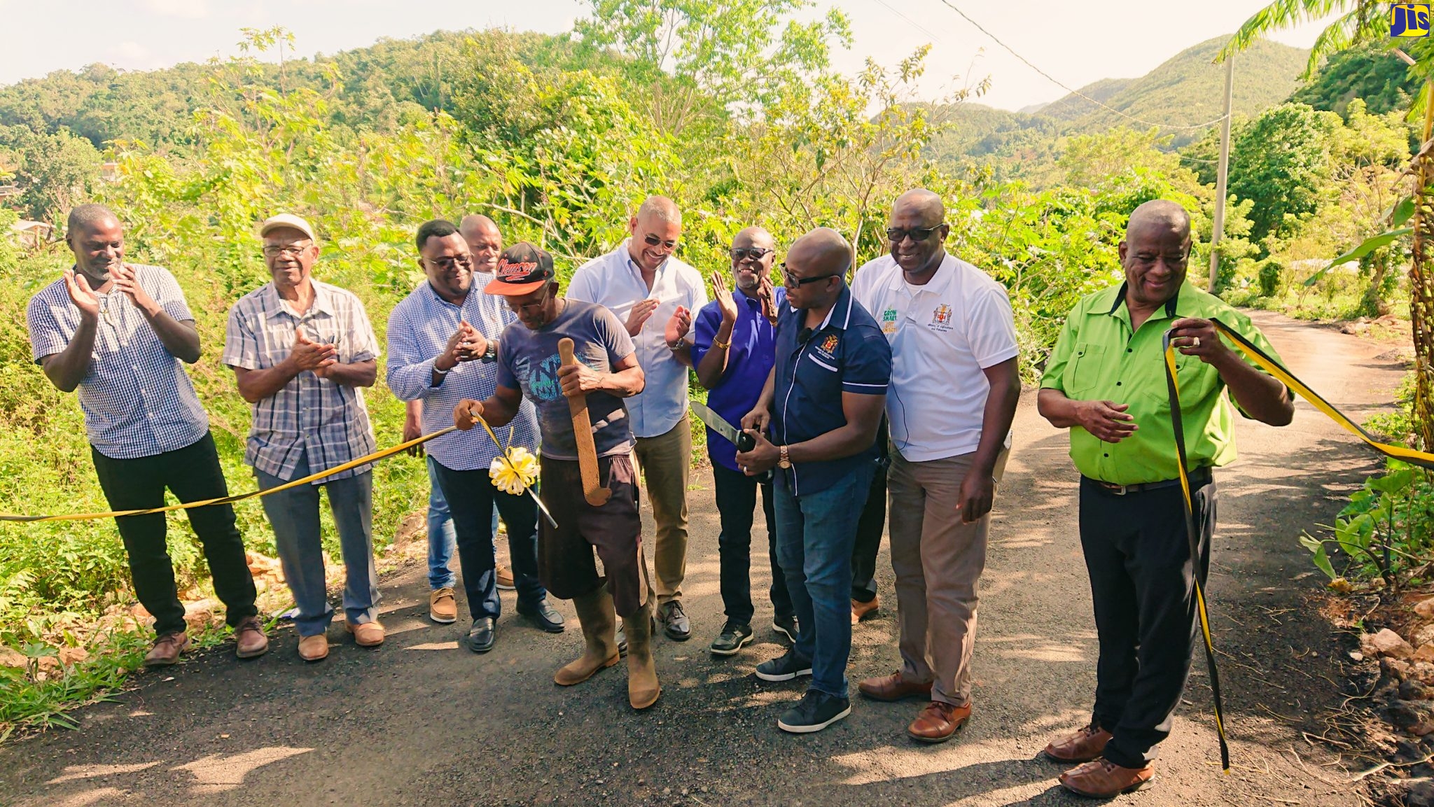 Minister of Agriculture and Fisheries, Hon. Pearnel Charles Jr. (third right), is assisted by Maidstone farmer Silburn Steadman (with machete) in cutting the ribbon to officially open the Grass Piece farm road in Manchester on Thursday (December 15). Among the other participants are Minister of State in the Ministry of Agriculture and Fisheries, Hon. Franklyn Witter (right); Member of Parliament, Manchester North Western, Mikael Phillips (fifth right), as well as representatives of the Rural Agricultural Development Authority (RADA). 