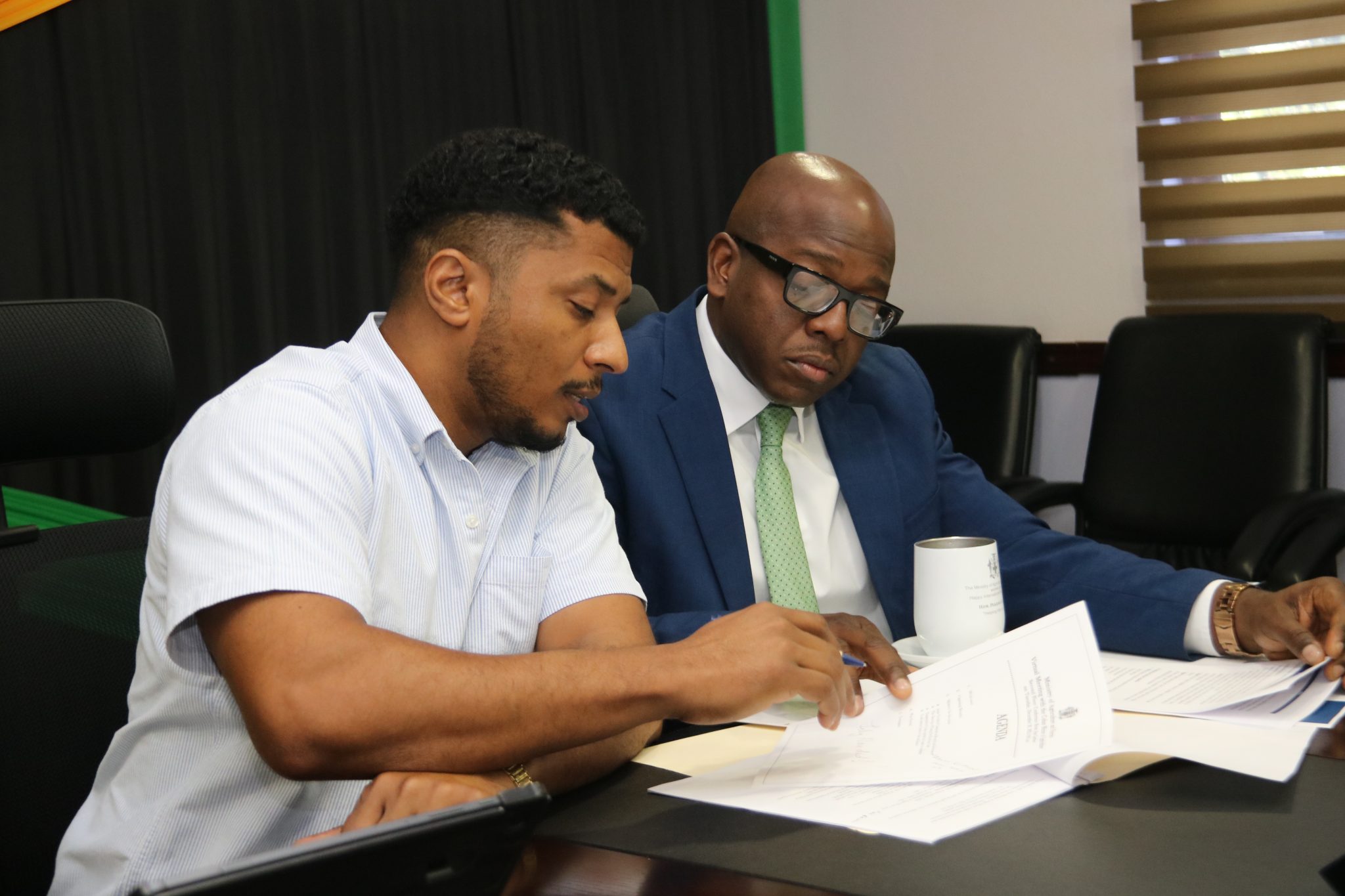 Minister of Agriculture and Fisheries,  the Hon. Pearnel Charles Jr (right), and Acting Principal Director of Agricultural Economic Planning & Policy, Kevin Condappa, peruse a document, during a virtual meeting with Cuba’s Deputy Minister of Agriculture,  Maury Hechavarria Bermudez, on December 20.