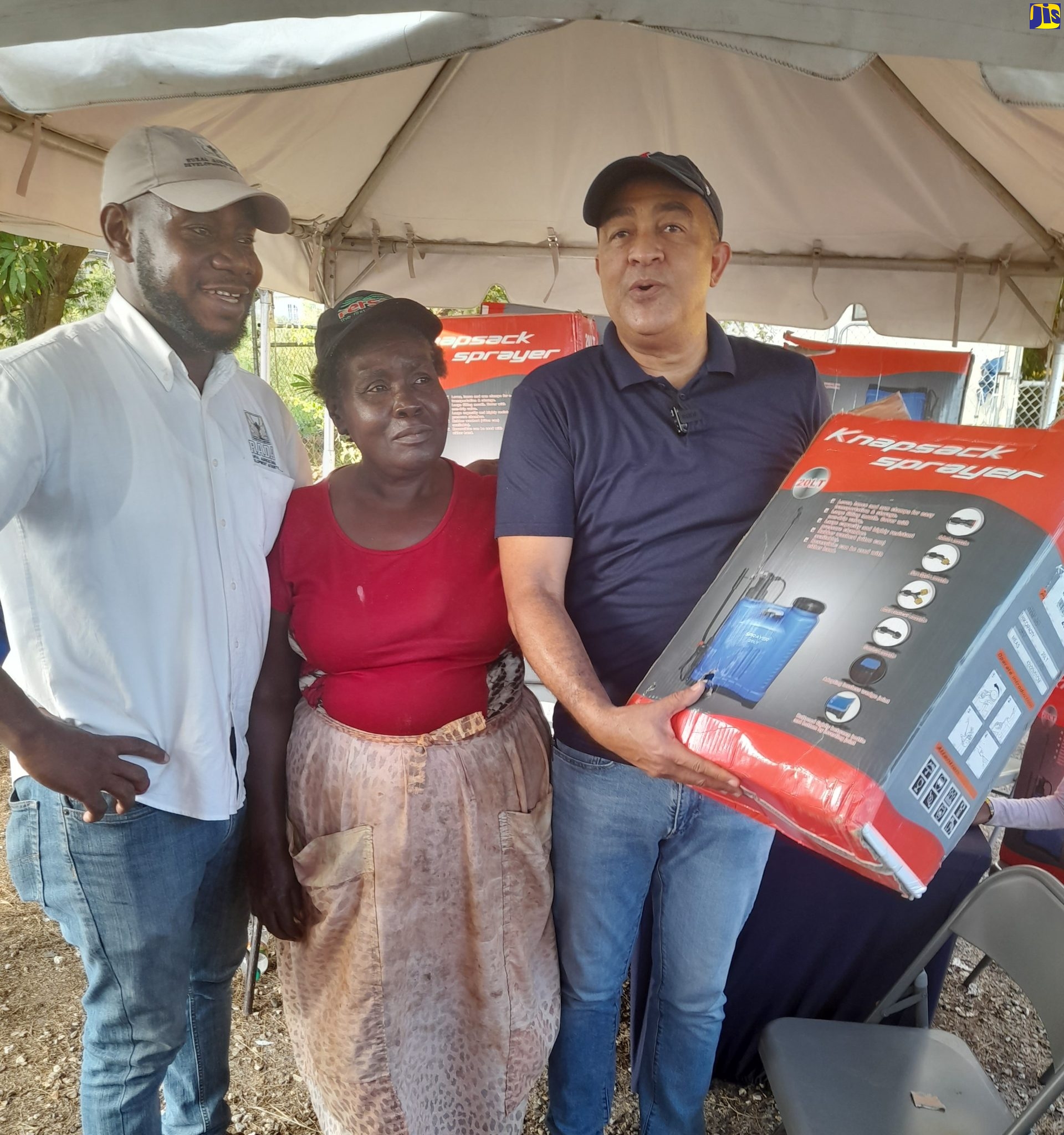 Member of Parliament for St. Catherine West Central, Dr. the Hon. Christopher Tufton (right), displays one of 30 knapsack sprayers presented to farmers, during a farmers’ market on Wednesday (December 21), at the Green Acres Commercial Complex in St. Catherine. Looking on (from left) are: Deputy Parish Manager for the Rural Agricultural Development Authority (RADA), Bryan Samuels; and farmer Amy Williams.