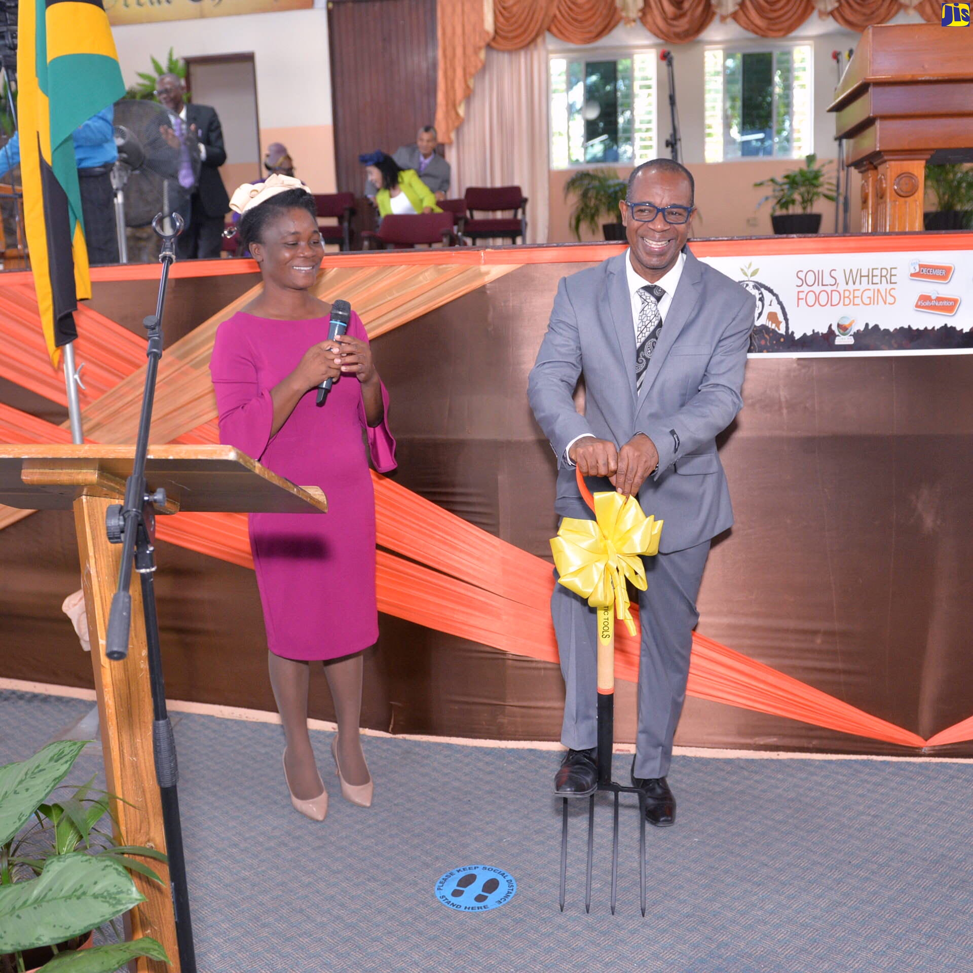 Pastor Leroy Laing of the Pentecostal Tabernacle on Wildman Street, has a light moment as he demonstrates the use of one of two pitch forks donated to the church by the Ministry of Agriculture and Fisheries. At left is Senior Director (Actg.), Agriculture and Land Division in the Ministry, Pamela McKenzie. Occasion the World Soil Day Church Service at  the church in Kingston on Sunday ( Dec. 4).