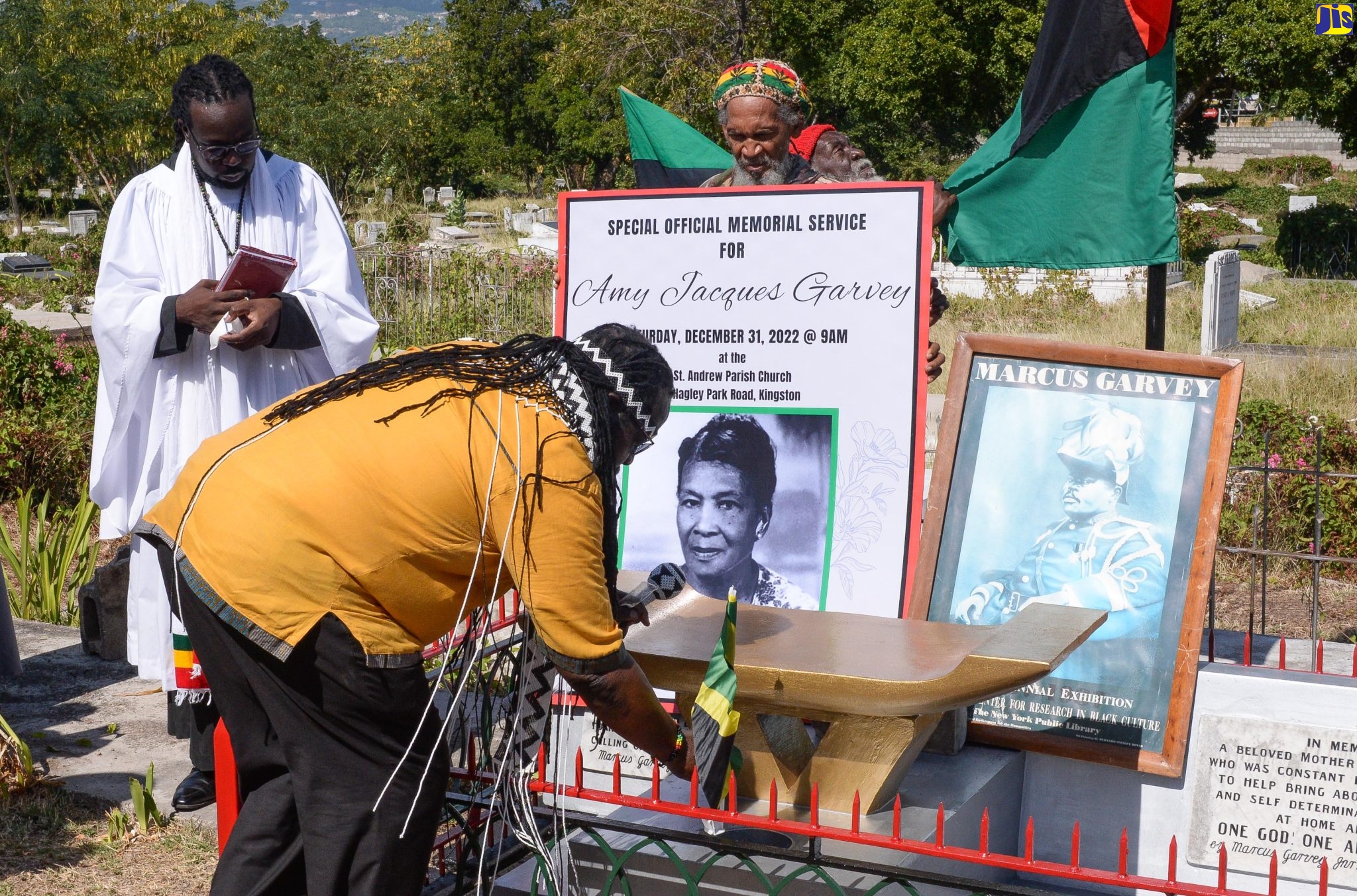 Claude “Big Stone” Sinclair (left), places a Jamaican flag on the grave of the late Amy Euphema Jacques Garvey, following a memorial service held at the St. Andrew Parish Church in Half-Way Tree on December 31. Looking on is Rev Fr Bertram Gayle.