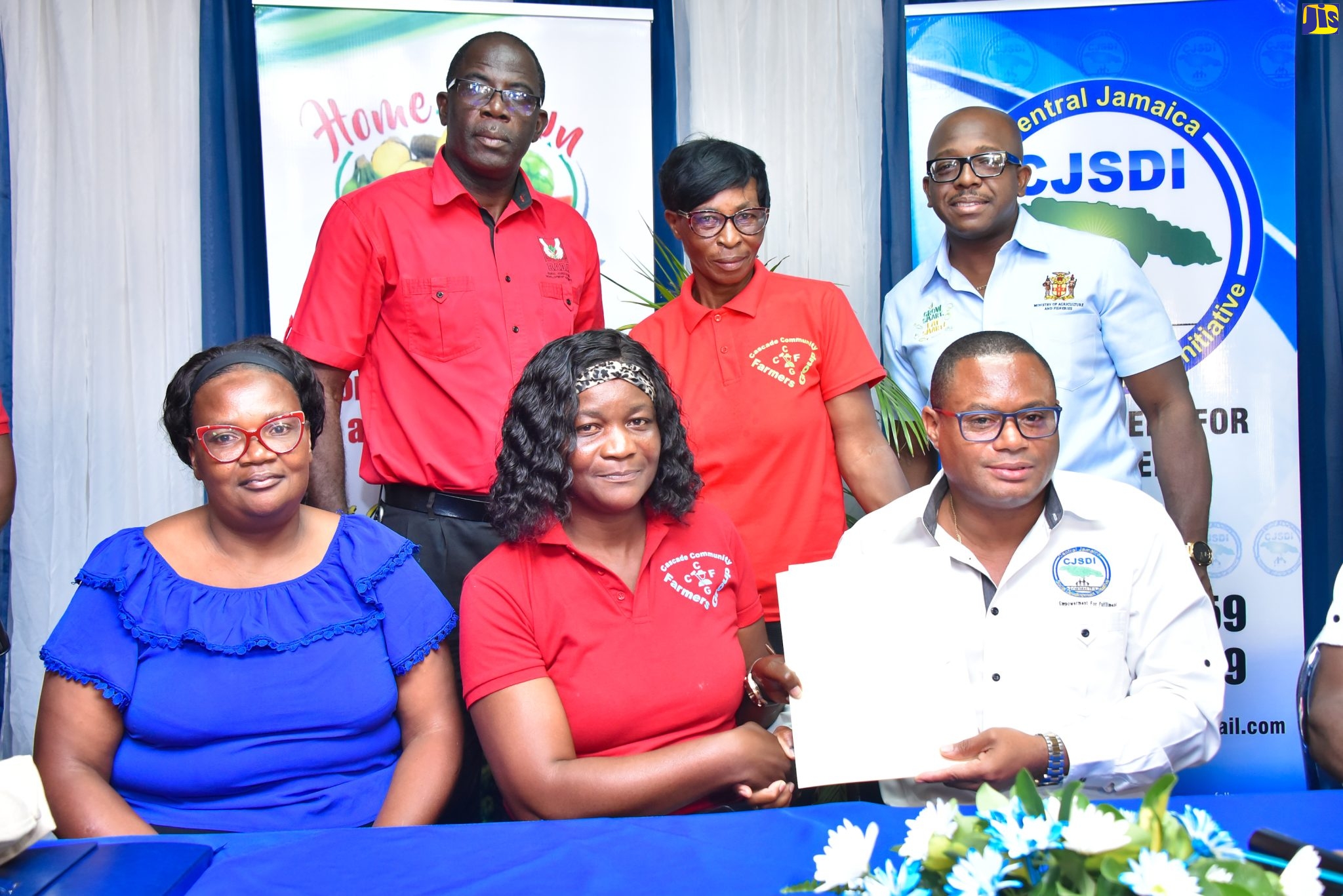 Minister of Agriculture and Fisheries, Hon. Pearnel Charles Jr. (standing, right,) looks on as Chief Executive Officer of Home Grown Produce, David Young (seated, right) and Cascade Community Farmers Group member, Thelma Watson (seated, centre), display a signed contract, during an Agri-Business Symposium on January 19 at the Tropics View Hotel in Manchester. Others sharing the moment (from left) are Davis Town Farmers Group member, Juliet Taylor;  Rural Agricultural Development Authority (RADA) Manchester Parish Manager, Winston Miller; and  Angella Walker from the Cascade Community Farmers Group.

