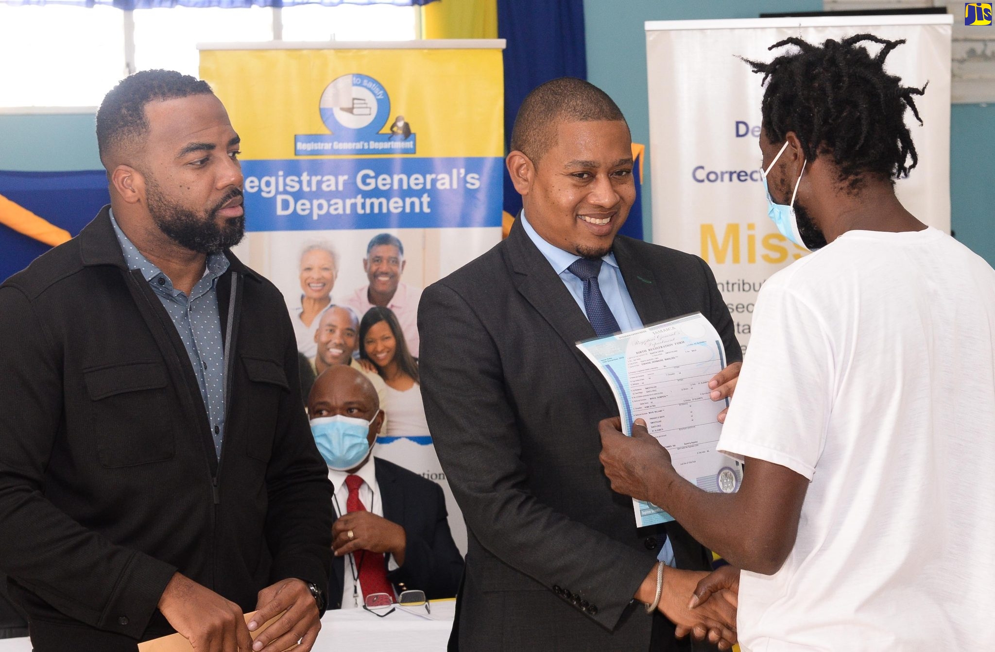 Minister Without Portfolio in the Office of the Prime Minister, Hon. Floyd Green (centre), hands over a free birth certificate under the ‘Operation Birthright’ project to an inmate of the St. Catherine Adult Correctional Centre, at the facility in Spanish Town, on Wednesday (February 15). Looking on is Chief Executive Officer and Deputy Keeper of Records, Registrar General’s Department (RGD), Charlton McFarlane.