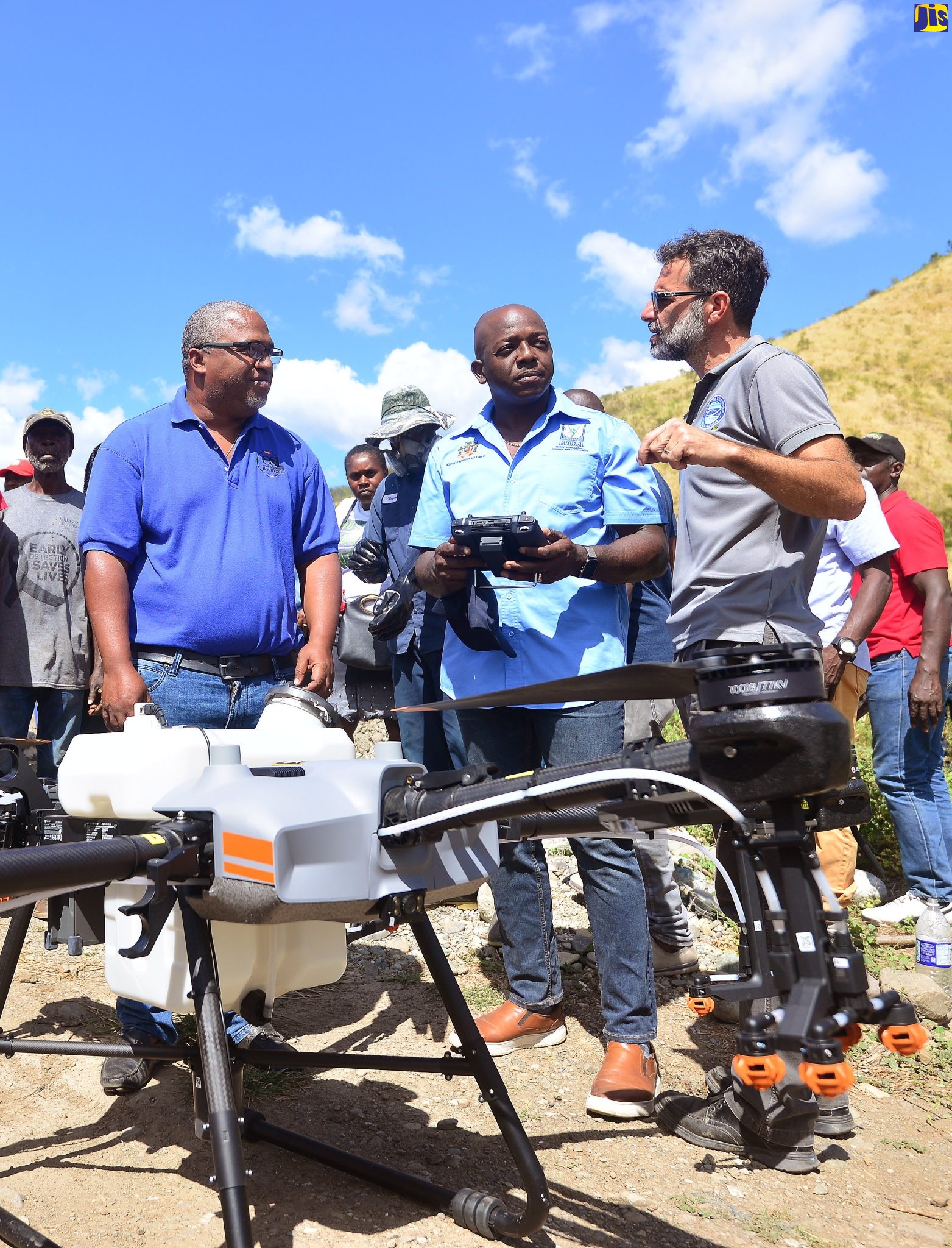 Minister of Agriculture and Fisheries, Hon. Pearnel Charles Jr. (centre), in discussion with Director of Agriculture and Fisheries at Food For the Poor, Nakhle Hado (right), while Chief Strategic Officer, Environmental Solutions Limited, Stephen Jones, looks on. They were in the process of observing a drone (foreground) being used to irrigate an onion farm in St. Thomas, during a tour on Thursday (February 16).