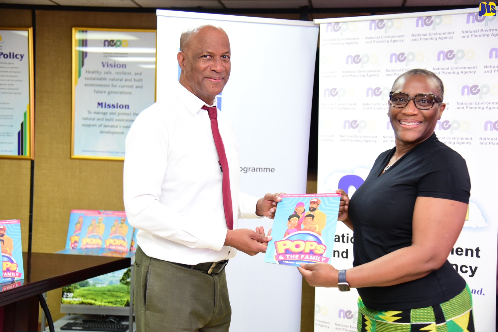 Director of Environmental Management, Conservation Division, National Environment and Planning Agency (NEPA), Anthony McKenzie, is presented with the educational children’s activity and colouring book ‘POPs and the Family’ by Resident Representative, United Nations Development Programme (UNDP), Denise Antonio. The book, which is intended for national distribution, is a specialised public-education product designed to help children identify and avoid persistent organic pollutants (POPs) commonly found in certain industries and substances in Jamaica. The handover ceremony was held on Thursday (March 9) at NEPA’s offices in Kingston. UNDP and NEPA are undertaking the public-education initiative as part of a comprehensive national project to reduce and eventually eliminate the importation, stockpiling and use of sources of POPs in Jamaica. POPs are present in widely used chemicals such as dielectric fluids in electrical equipment, flame retardants and pesticides. Exposure to POPs is hazardous to human health and has been linked to chronic illnesses, certain cancers, birth defects, and dysfunctional immune and reproductive systems.
