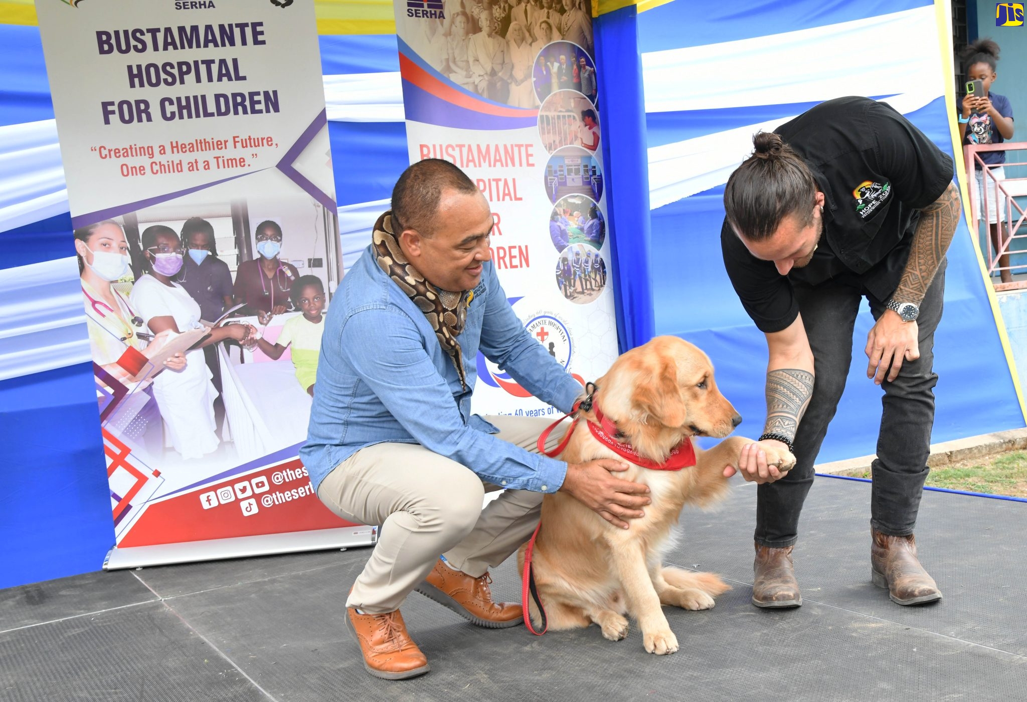 Minister of Health and Wellness, Dr. the Hon. Christopher Tufton (left) and trainer and curator at the Hope Zoo, Joseph Brown, interact with golden retriever “Dr. Teddy Barks”, who is the main therapy animal under the Animal-Assisted Recovery and Care Pilot Project at the Bustamante Hospital for Children.  Occasion was the official launch of the project on Tuesday (March 28) at the hospital in Kingston.