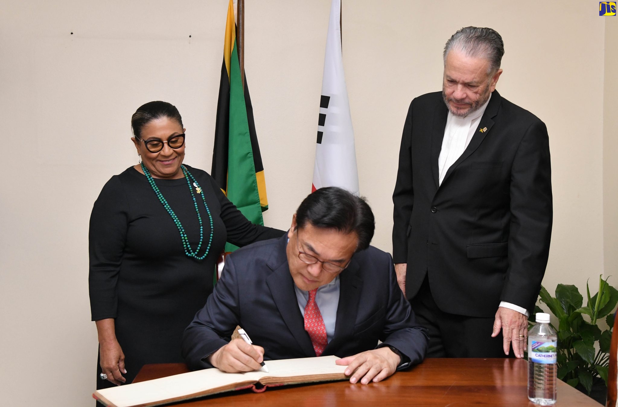 Speaker of the House of Representatives, Marisa Dalrymple-Philibert (left) and President of the Senate, Senator the Hon. Thomas Tavares-Finson (right) look on as President of the Korea-Jamaica Parliamentary Friendship Group, Chung Jin-suk, signs the guest book during the visit to Gordon House on April 19.