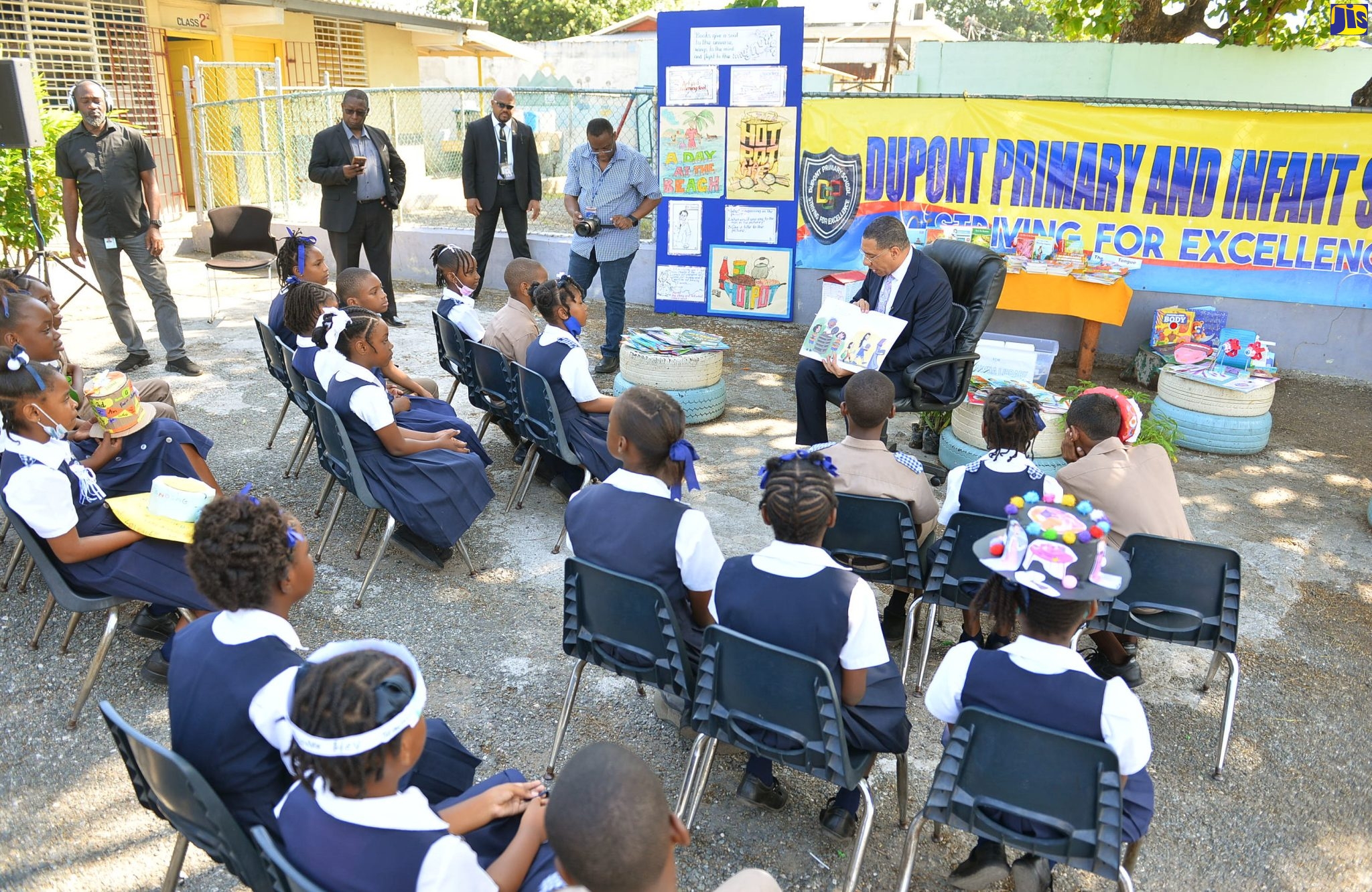 Prime Minister, the Most Hon. Andrew Holness (right, seated), points to illustrations in the book ‘I Can Do My Part’, by Cathryn O’Sullivan, while reading to grade-four students at Dupont Primary and Infant School. The occasion was a visit to the institution, located in his St. Andrew West Central constituency, as part of activities marking Read Across Jamaica Day on Tuesday (May 9).  