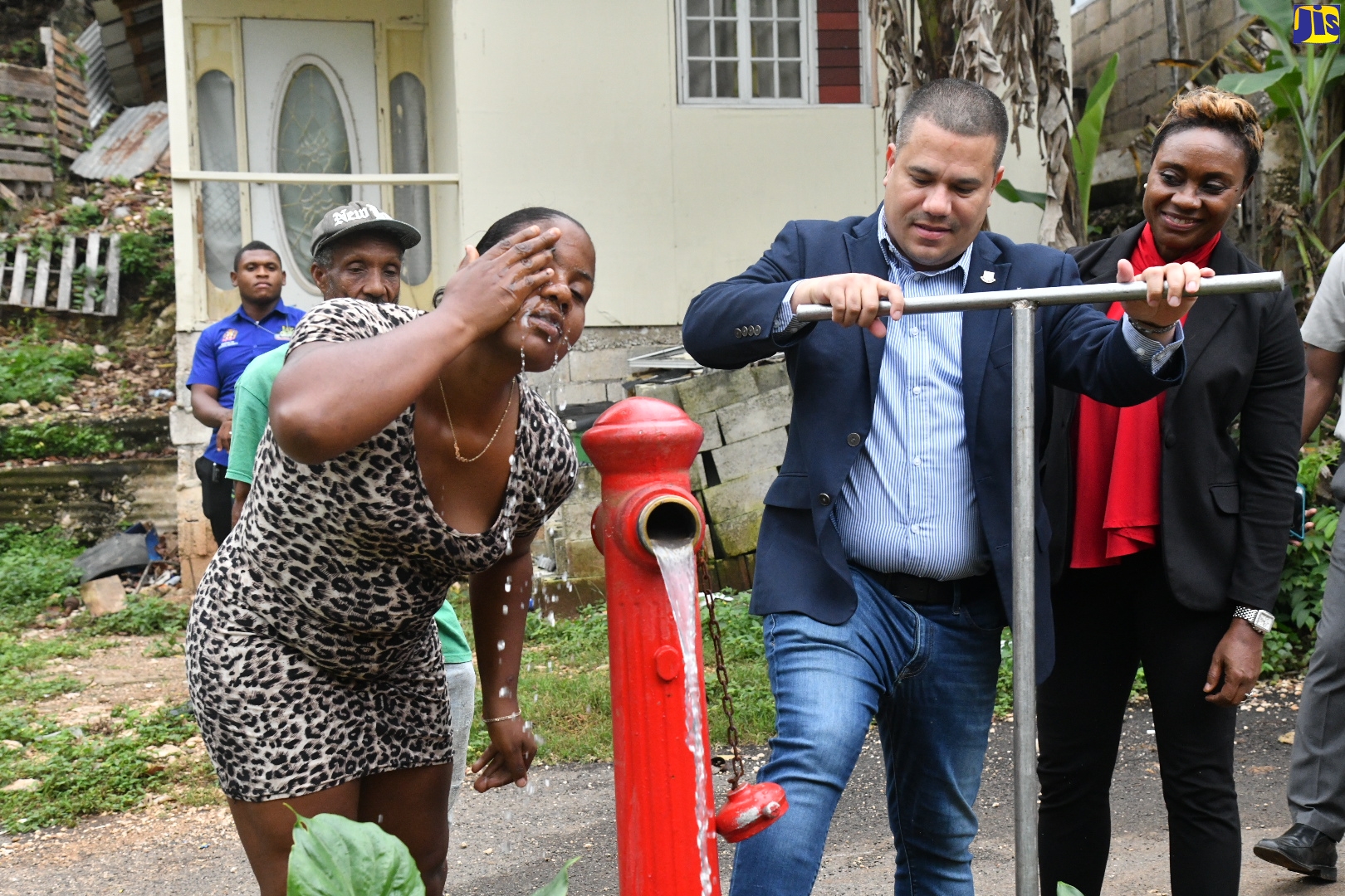 Water pours from a fire hydrant turned on by Minister Without Portfolio in the Ministry of Economic Growth and Job Creation, Senator the Hon. Matthew Samuda (centre), while resident of Sterling Castle Heights, St. Andrew, Suzanne Thompson (left), splashes some on her face. Occasion was the commissioning into service of a recently completed pipeline replacement project and upgrading works in the community on June 8.  Looking on at right is Member of Parliament for West Rural St. Andrew, Hon. Juliet Cuthbert- Flynn.