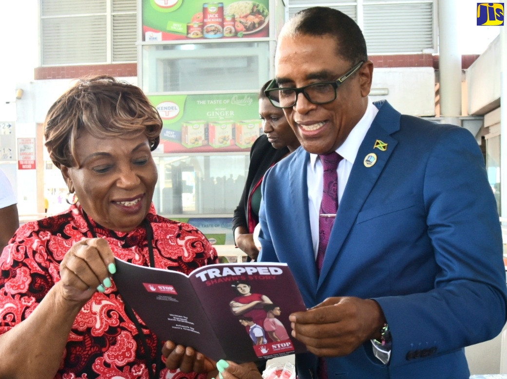Minister of State in the Ministry of Labour and Social Security, Dr. the Hon. Norman Dunn (right); and member of the National Task Force Against Trafficking in Persons (NATFATIP), Ministry of National Security, Audrey Budh, look at a booklet during the ‘World Day Against Child Labour’ Information Blitz on June 12 at the Half-Way Tree Transport Centre in St. Andrew.