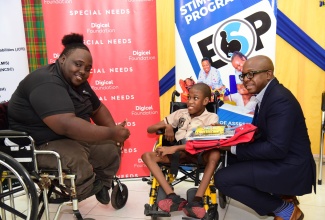 Minister of Labour and Social Security, Hon. Pearnel Charles Jr. (right), presents special needs student Delano Clarke (centre) with school supplies donated by Digicel Foundation at Stimulation Plus Child Development Centre on Hanover Street in downtown Kingston on Monday (August 21). Sharing in the presentation is Digicel Education and Special Needs Project Officer, Jeneard Williamson.