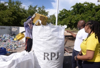 Recycling Partners of Jamaica (RPJ) General Manager, Gairy Taylor (centre), and National Solid Waste Management Authority (NSWMA) Community Relations Manager, Kimberly Blair (right), observe as an RPJ employee deposits plastic bottles into a bag during a cleanup of the New Causeway Fishing Village in St. Catherine on July 5. The NSWMA partnered with RPJ to clear the fishing village of plastic bottles and debris in observance of Plastic Free July.