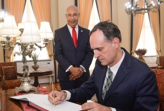 Governor-General, His Excellency the Most Hon. Sir Patrick Allen (left), observes as outgoing Ambassador of Belgium to Jamaica, His Excellency Hugo Verbist, signs the guest book at Kings House during the diplomat’s farewell courtesy call on Thursday (July 13).