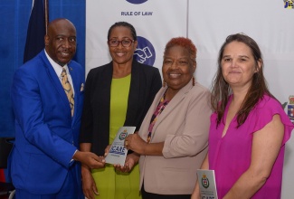 Reverend Courtney Faulknor (left) from the Jamaica Constabulary Force’s (JCF) Chaplaincy, accepts a copy of a Domestic Violence Handbook from Representative of the United Nation’s Population Fund (UNFPA) for the English and Dutch-speaking Caribbean, Elizabeth Talbert (second right). The handover took place during the graduation ceremony for the Domestic Violence Intervention Centre’s (DVIC) Domestic Violence Train-the-Trainer Course, at the National Police College of Jamaica (NPCJ) in St. Catherine on Friday (July 21). Sharing the moment are Head of the JCF’s Community Safety and Security Branch, Assistant Commissioner of Police (ACP), Charmine Shand (second left), and Gender-Based Specialist, UNFPA, Elga Salvador.