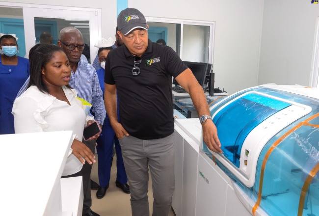 Health and Wellness Minister, Dr. the Hon. Christopher Tufton (right), listens as Medical Technologist at the Spanish Town Hospital, Venetia Oakley (left), outlines the features of new lab testing machine during a tour of the hospital grounds in St. Catherine on August 9. Looking on (at centre) is Board Chairman, South East Regional Health Authority (SERHA), Wentworth Charles.