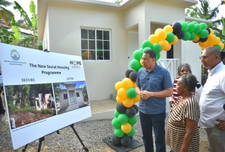 Prime Minister, the Most Hon. Andrew Holness (left), and New Social Housing Programme (NSHP) beneficiary, Barbara Johnson (centre), and Manchester North Western Member of Parliament, Mikhail Phillips, view pictures of her burnt out house in St. Paul’s, Manchester, and the new unit built under the NSHP to replace it. Prime Minister Holness presented the keys for the new three-bedroom house to Ms. Johnson on Friday (July 14).