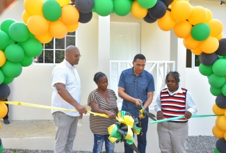 Prime Minister, the Most Hon. Andrew Holness (second right), cuts the ribbon prior to formally presenting the keys for a new three-bedroom house to resident of St. Paul’s, Manchester, Barbara Johnson (second left). The home was built under the New Social Housing Programme (NSHP). Looking on (from left) are Manchester North Western Member of Parliament, Mikhail Phillips, and Principal Finance Officer, Ministry of Economic Growth and Job Creation, Judith Robb-Walters, who chairs the NSHP Oversight Committee