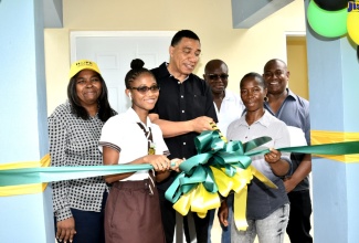 Prime Minister the Most Hon. Andrew Holness (third left), cuts the ribbon symbolising the official handover of a two-bedroom house to Georgette Moving (second right) at Bamboo Ridge, Bartons, St. Catherine South Western, recently. The house was built at a cost of $5 million under the New Social Housing Programme (NSHP). Sharing the moment (from left) are Chairman, Oversight Committee, NSHP, Judith Robb Walters; Ms. Moving’s daughter, Janelle Evans; Minister without Portfolio in the Ministry of Economic Growth and Job Creation and St. Catherine South Western Member of Parliament, Hon. Everald Warmington and Councillor, Old Harbour North, Keith Knight.