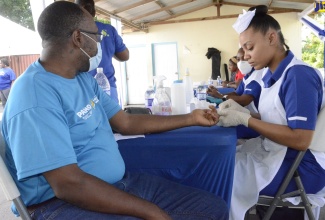 MDH: Parish Health Promotion and Education Officer at the Westmoreland Health Department, Gerald Miller (left), gets his blood sugar checked by student nurse Loshane Dell (right) during a Men’s Health Day fair at the Savanna-la-Mar Health Centre in Westmoreland on June 30.