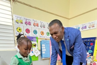 Chief Executive Officer, Culture, Health, Arts, Sports and Education (CHASE) Fund, Wilford “Billy” Heaven, admires a truck made from juice boxes by Savanna-la-Mar Infant School student, Leana Barker.
