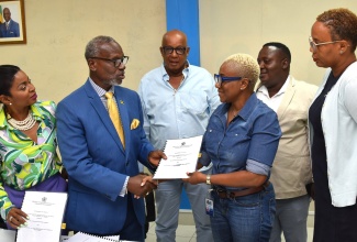 Minister of Local Government and Community Development, Hon. Desmond McKenzie (second left), hands over the contract for the upgrade of Hill Sixty Road in Cheswick, St. Thomas, to Director, FSC Construction Works Limited, Karen Cameron (third right). The signing ceremony for the $12.8-million project took place at the Ministry’s Hagley Park Road offices in St. Andrew on July 18. Others sharing in the moment (from left) are Member of Parliament, St. Thomas Eastern, Dr. Michelle Charles; Councillor, Dalvey Division, Michael McLeod; Mayor of Morant Bay, Councillor Hubert Williams and Acting Chief Executive Officer, St. Thomas Municipal Corporation, Tamika Small.