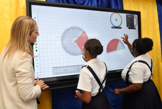 Sales Education Consultant for Promethean, South Florida and the Caribbean, Amanda Leich (left), looks on as Titchfield High School students, Zerena Davis (right) and Sherona Kirkland, use the company’s ActivPanel Interactive Display, which was handed over to the institution in Portland on June 29.
