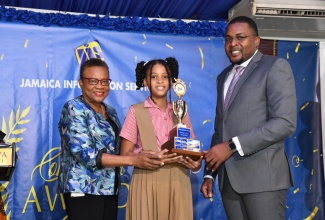 Minister without Portfolio in the Office of the Prime Minister with Responsibility for Information, Hon. Robert Morgan (right), and Chief Executive Officer, Jamaica Information Service (JIS), Enthrose Campbell (left), present JIS Heritage Essay Competition winner, Shadair Green, with her prizes, during the JIS’s 2022 Heritage Competition Awards Ceremony at the Terra Nova All-Suite Hotel in St. Andrew.

