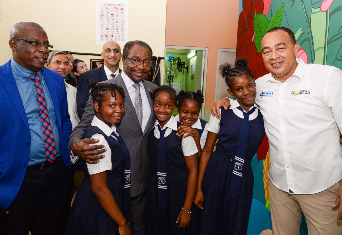 Minister of Health and Wellness, Dr. the Hon. Christopher Tufton (right); Parish Manager for St. Catherine Health Services, Abdon Campbell (left), and United States (US) Ambassador to Jamaica, His Excellency N. Nick Perry (centre),  with students from the Linstead Primary School, during the official opening of a child-friendly space at the Ewarton Health Centre, in St. Catherine, on November 15.