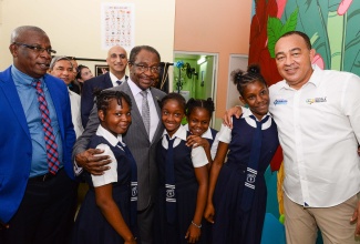 Minister of Health and Wellness, Dr. the Hon. Christopher Tufton (right); Parish Manager for St. Catherine Health Services, Abdon Campbell (left), and United States (US) Ambassador to Jamaica, His Excellency N. Nick Perry (centre),  with students from the Linstead Primary School, during the official opening of a child-friendly space at the Ewarton Health Centre, in St. Catherine, on November 15.