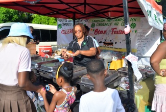 Parish Secretary, Kingston 4-H Clubs, Georgia McPherson (centre) serves stew June plum to a patron at the Lauriston/Thompson Pen Community 4-H Club stew festival, held at Brooklyn Park in Spanish Town, St. Catherine on November 4.