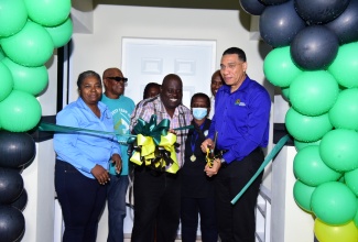 Prime Minister the Most. Hon. Andrew Holness (right) cuts the ribbon to mark the handover of a two-bedroom house, built under the New Social Housing Programme (NHSP), to Rhoel Clarke (centre), in James Hill, Clarendon on Friday (December 15). Looking on is Chairperson for the Oversight Committee of the NSHP, Judith Robb Walters (left).