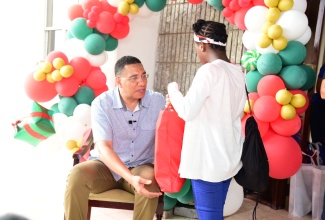Prime Minister, the Most. Hon. Andrew Holness (left) presents Christmas gifts to a child in State care, during his annual treat for children, which was held on the grounds of the Office of the Prime Minister on Sunday (December 17).