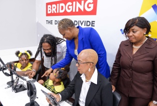 Minister of Education and Youth, Hon. Fayval Williams (second right), tries out a tablet in the smartroom at the St. Catherine-based Homestead Primary and Infant School, while Regional Director with the Ministry, Sophia Forbes Hall (right), observes. Occasion was the official opening of the facility on Wednesday (December 6), which was established by the Digicel Foundation at a cost of US$60,000.  Social Development Consultant with the Digicel Foundation, Miguel Williams (second left), and Principal of the school, Sophia Deer (third right), show students, Leandra Lawrence (right) and Shanoya Samuels, how to operate the devices.

