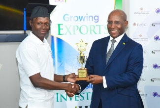 Minister of Industry, Investment and Commerce, Senator the Hon. Aubyn Hill (right), presents a trophy to the top student, Recardo McLarty from Sagility business process outsourcing company. Occasion was the graduation ceremony for supervisors in the global services sector held on December 6 at the Jamaica Promotions Corporation (JAMPRO) in Kingston.

