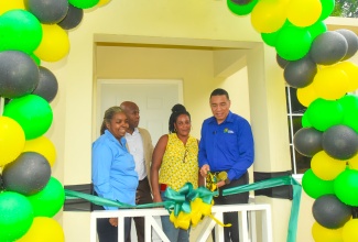 Prime Minister, the Most Hon. Andrew Holness (right), cuts the ribbon to mark the handover of a two-bedroom house, built under the New Social Housing Programme (NHSP), to Bridget Brown  (second right) in Morgan’s Forrest, Clarendon on Friday (December 15). Looking on (from left) are Chairperson for the Oversight Committee of the NSHP, Judith Robb Walters; and Member of Parliament for Clarendon Northern, Dwight Sibblies.